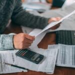 Newsom’s Tax Return Rollout Draws Sharp Criticism Person reviewing bills with calculator at cluttered desk