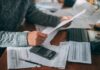 154,000 Workers Put on Leave Person reviewing bills with calculator at cluttered desk