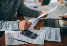 Person reviewing bills with calculator at cluttered desk