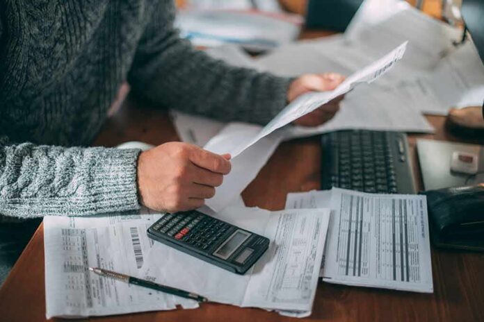 Person reviewing bills with calculator at cluttered desk