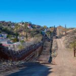 Border fence with barbed wire along a dirt road in hilly terrain