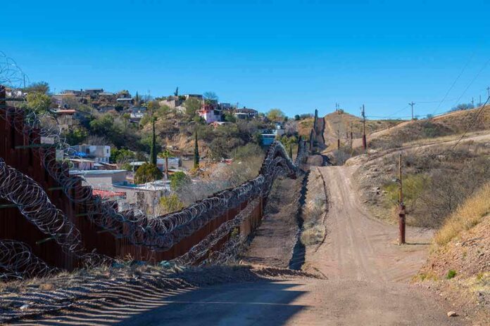 shutterstock_2408010203 Border fence with barbed wire along a dirt road in hilly terrain