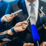 Man in suit surrounded by microphones at press conference