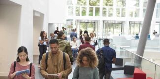 Students walking through a bright campus lobby using mobile devices
