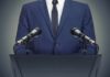 Speaker in suit at podium with two microphones