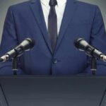 Speaker in suit at podium with two microphones