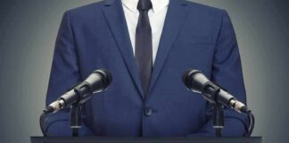 Speaker in suit at podium with two microphones