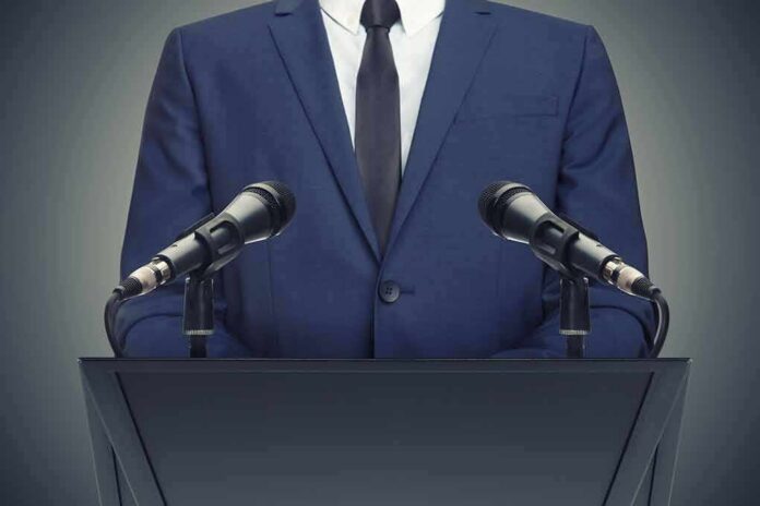Speaker in suit at podium with two microphones