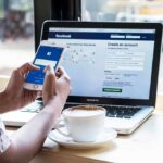 Parents Could Lose 4 Days of Summer to Phone Scrolling Hands using smartphone with laptop and coffee on cafe table