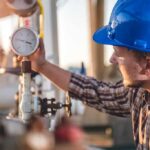 Engineer in blue hard hat checking a pressure gauge