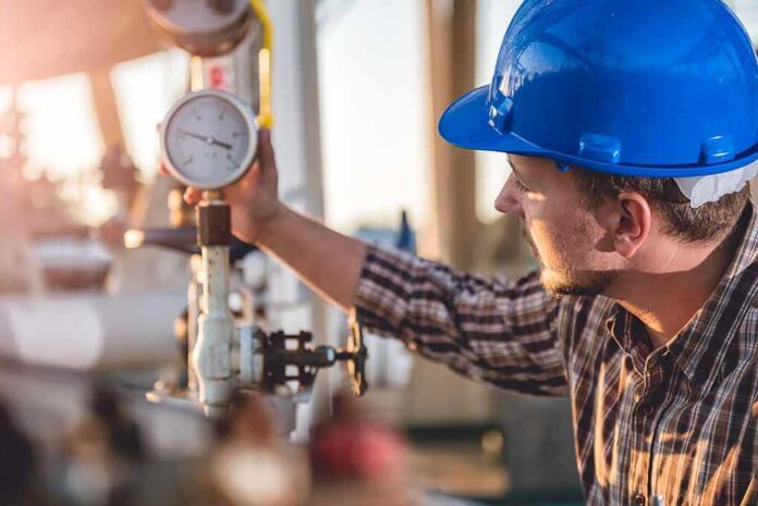 Engineer in blue hard hat checking a pressure gauge
