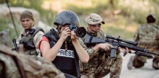 Teddy Williams photographing near armed soldiers in a field