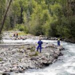 Missing Tubers Found Alive After Three Days Rescue workers in helmets standing along a fast-flowing forest river
