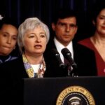 New Press Secretary Faces Scrutiny After Brief Debut Federico Peña stands behind a woman speaking at a podium with the presidential seal