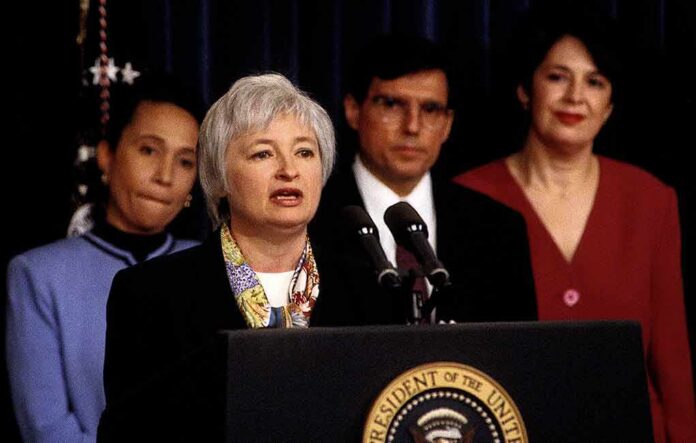 shutterstock_1084185701 Federico Peña stands behind a woman speaking at a podium with the presidential seal