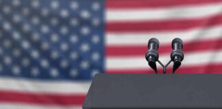Podium with microphones in front of a blurred American flag