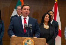 Florida Republicans Clash Over Candidate Ron DeSantis speaking at a podium with Chi Onwurah standing behind him