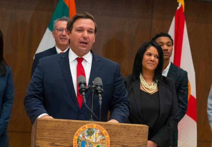 shutterstock_1355382878-2 Ron DeSantis speaking at a podium with Chi Onwurah standing behind him