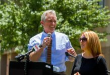 Robert F. Kennedy Jr. speaking at an outdoor podium with a woman beside him