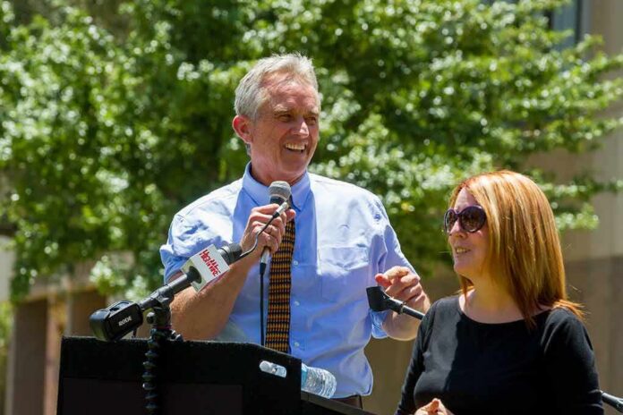 shutterstock_1401964070 Robert F. Kennedy Jr. speaking at an outdoor podium with a woman beside him