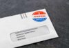 Absentee ballot envelope with I Voted sticker on dark surface