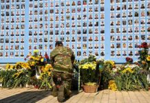 Israel Holds State Memorial for October 7 Victims Soldier kneels at memorial wall with photos and flowers