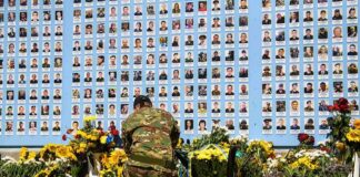 Soldier kneels at memorial wall with photos and flowers