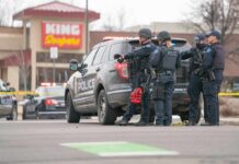 Police Respond Within Minutes to School Shooting Police officers gather beside a patrol SUV at a taped-off scene