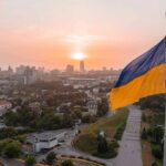 Ukrainian flag flying over a city at sunset