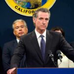 Gavin Newsom at a podium during a press conference with officials behind him