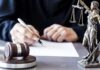 Pipe Bomb Suspect’s “Yes” Faces Court Scrutiny Judge writing at desk with gavel and Lady Justice statue